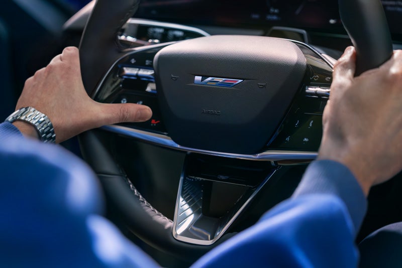 Close-up of a Man About to Press the V-Button on the 2026 OPTIQ-V Steering Wheel | Coughlin Cadillac Circleville in Circleville OH